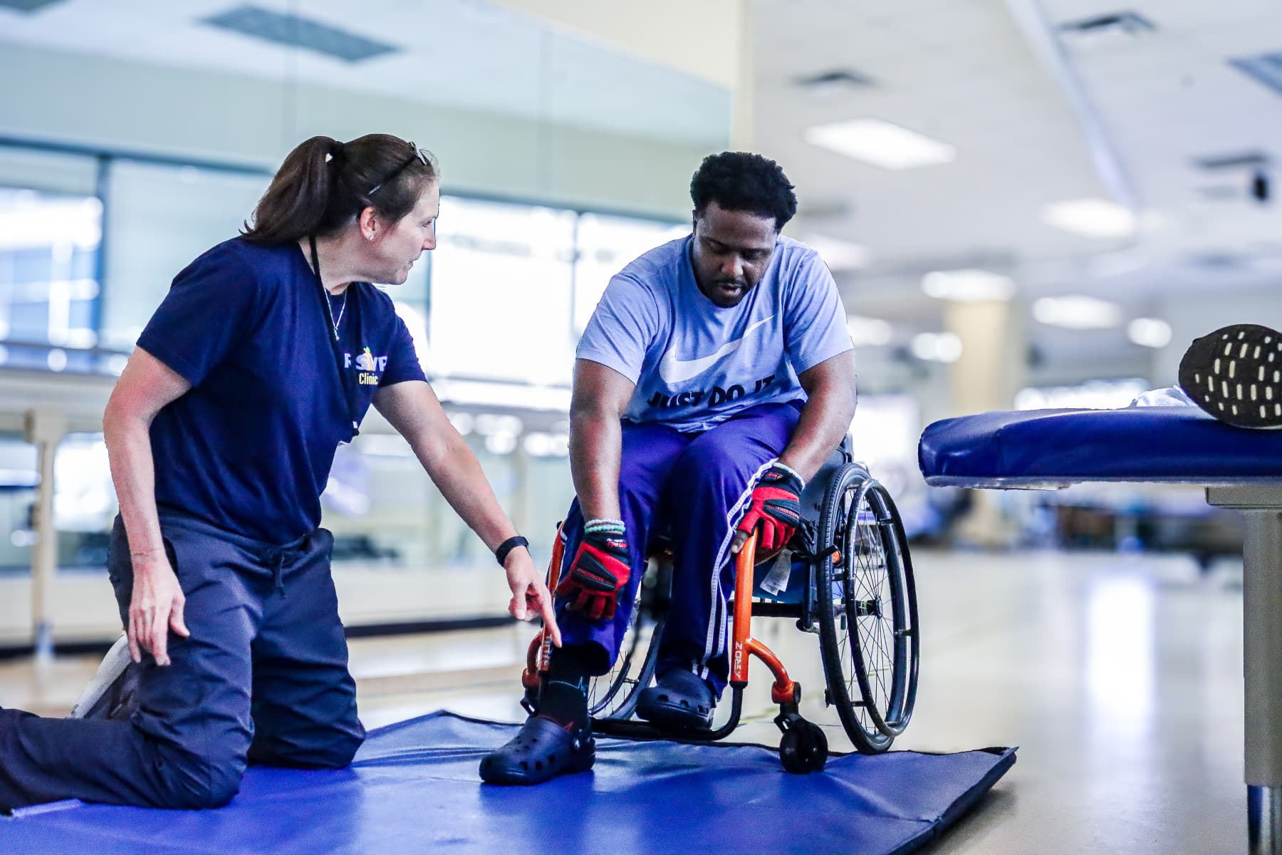 A wheelchair user and a therapist working through a floor transfer in a rehab gym