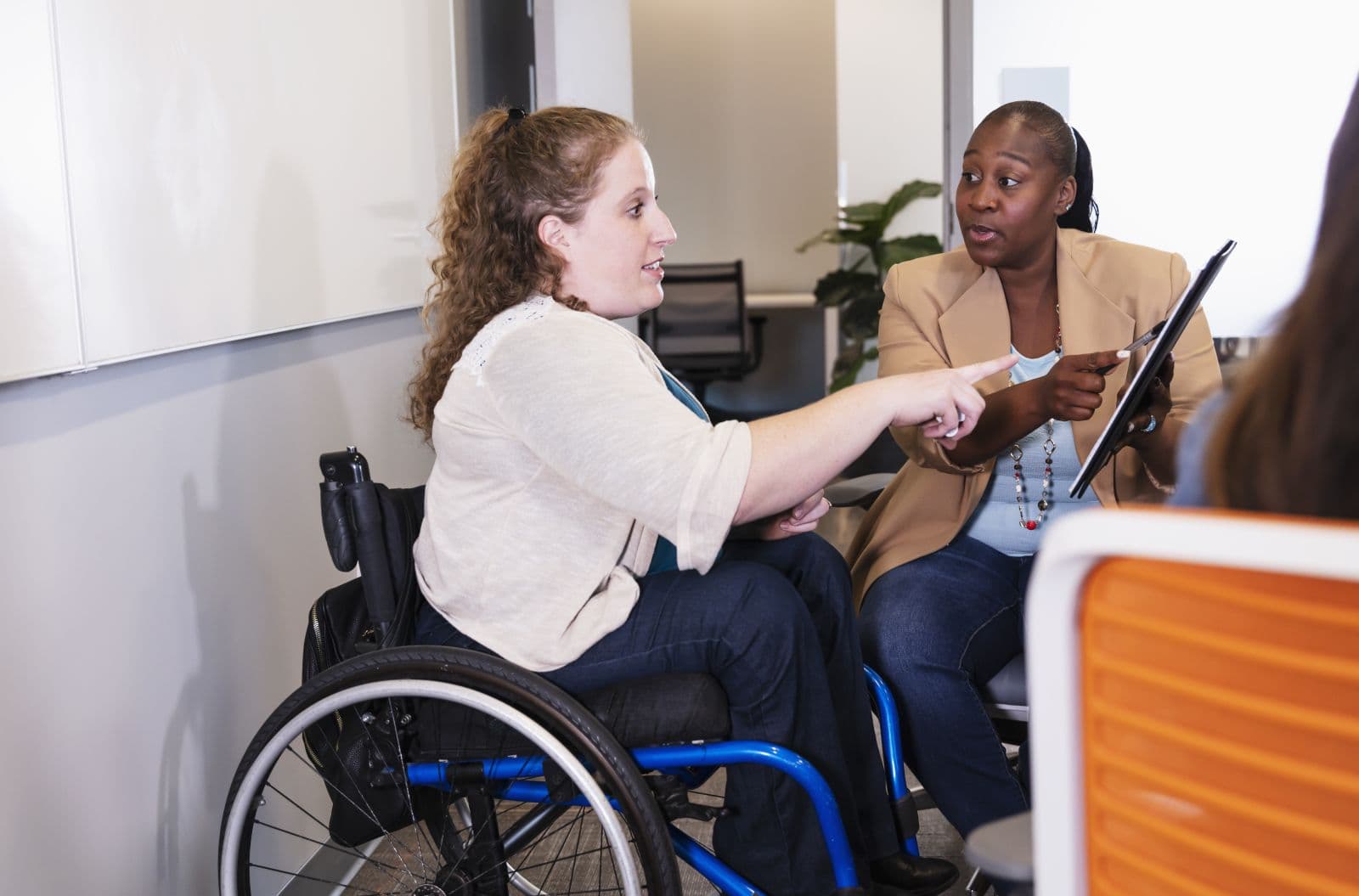 Two wheelchair users in conversation reviewing notes on a tablet