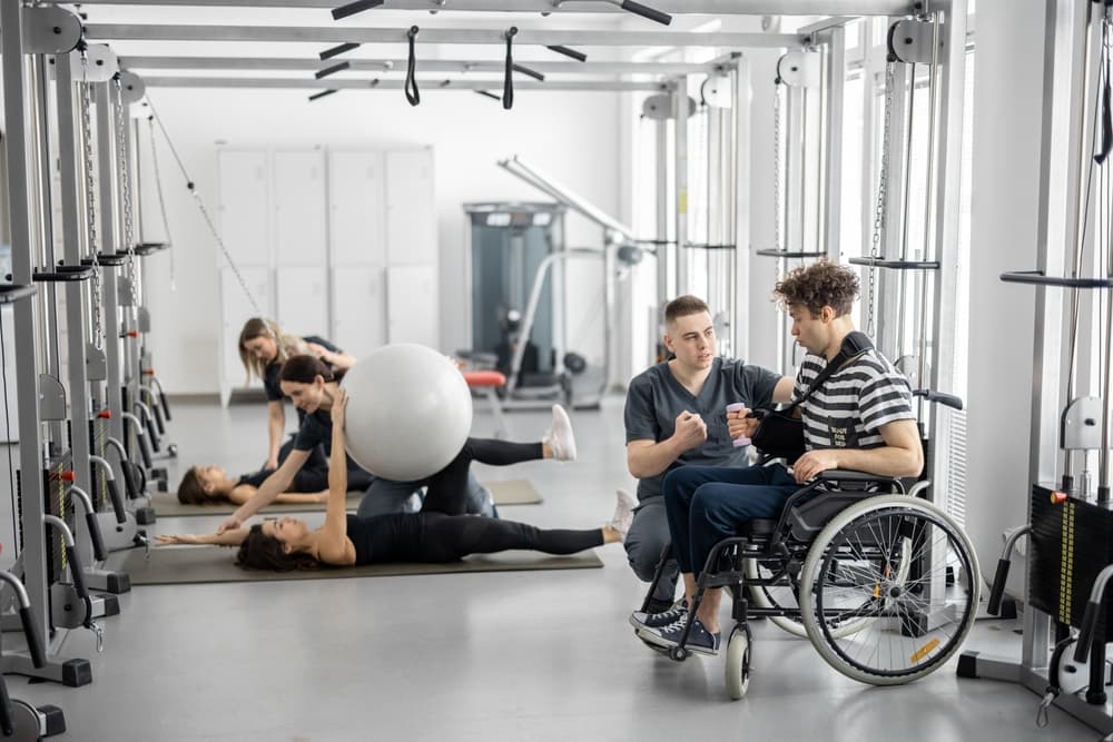 A physical therapist kneeling beside a wheelchair user, both smiling during a session